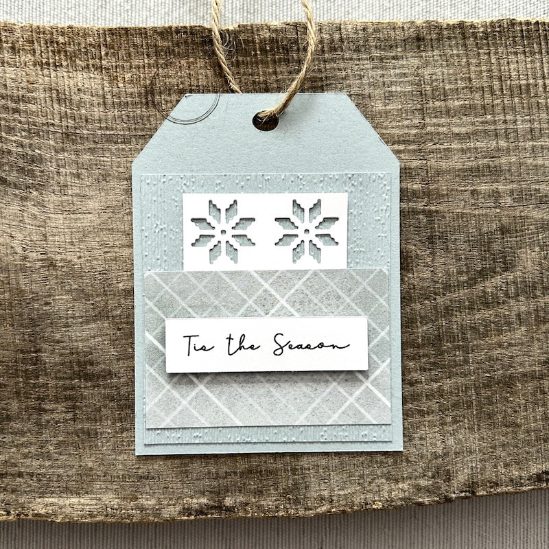 A finished tag, from this gift tag kit, sitting on a wooden board.