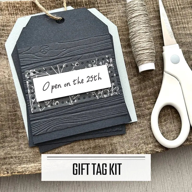 A DIY gift tag kit for Christmas. A finished tag is sitting on blank tags with a roll of twine and scissors.