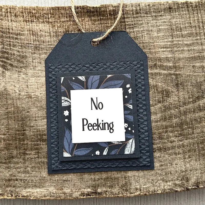 A finished tag, from this gift tag kit, sitting on a wooden board.