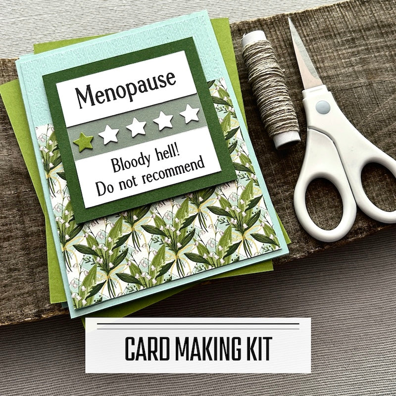 A DIY card making kit for funny menopause cards. A finished card is sitting on blank cards with a roll of twine and scissors.