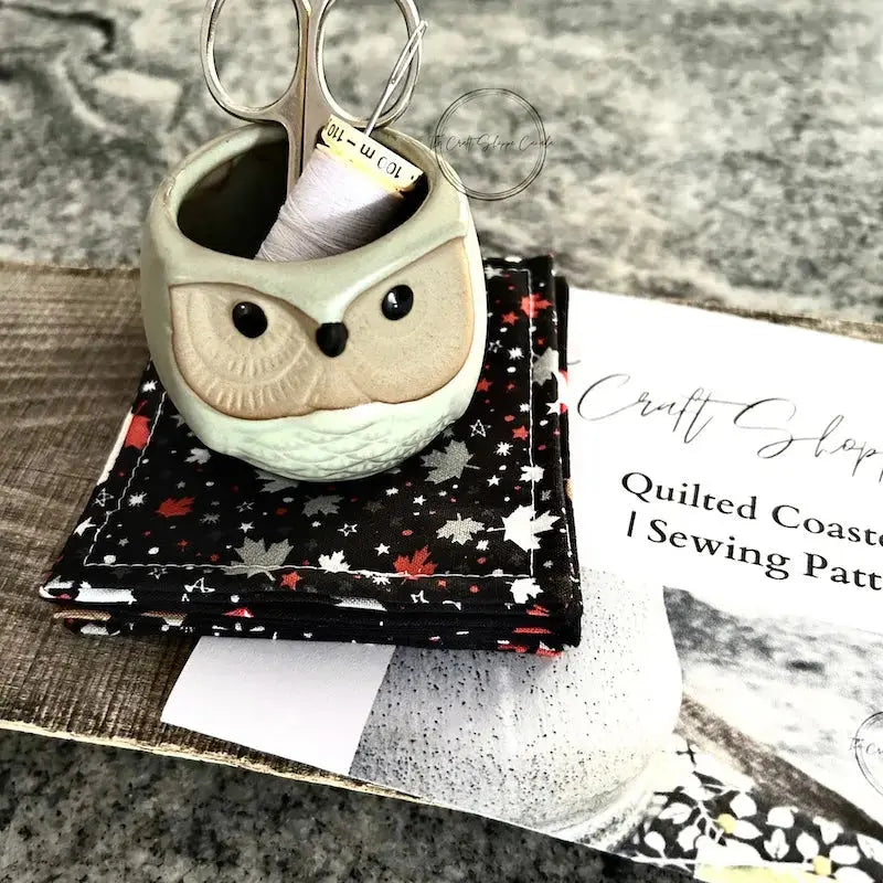 The finished coaster set is sitting on a wooden board with the sewing pattern, scissors and a spool of thread.