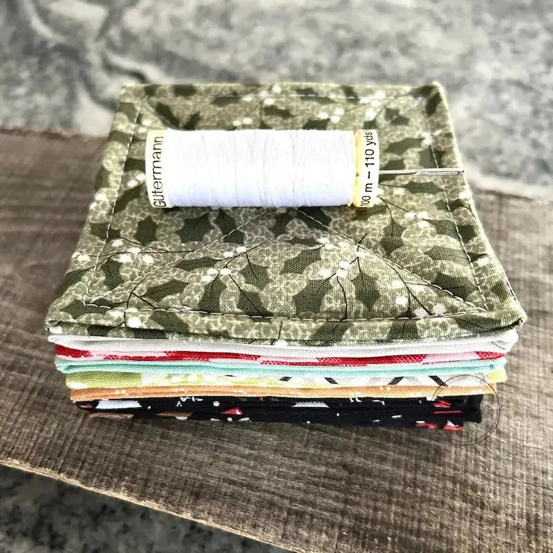 A spool of thread is sitting on a stack of finished coasters, made from this sewing pattern.