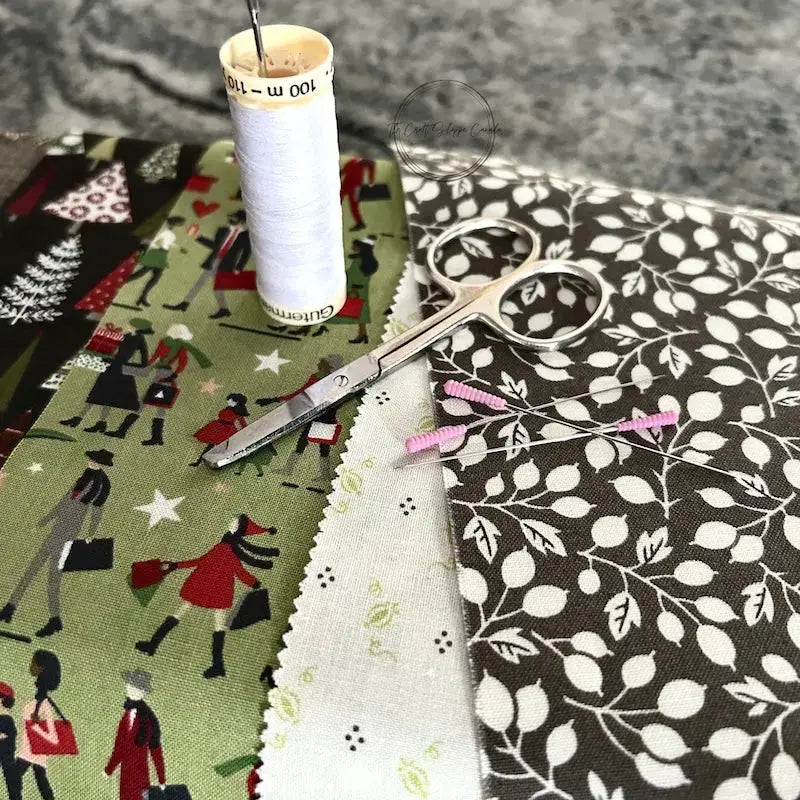 A spool of thread, scissors and sewing pins are sitting on a wooden board with the fabric used in this sewing kit.