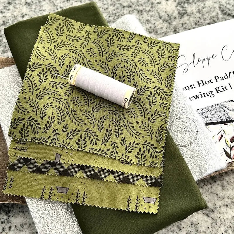 The pattern for this sewing kit is lying on a wooden board with fabric, a spool of thread and a hand sewing needle.