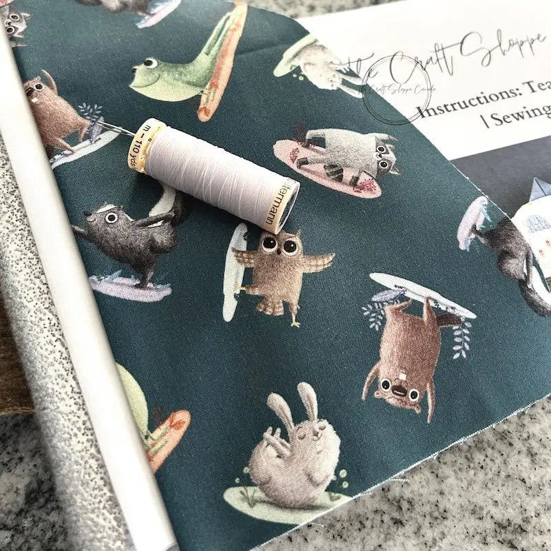 The pattern for this sewing kit is lying on a wooden board with fabric, a spool of thread and a hand sewing needle.