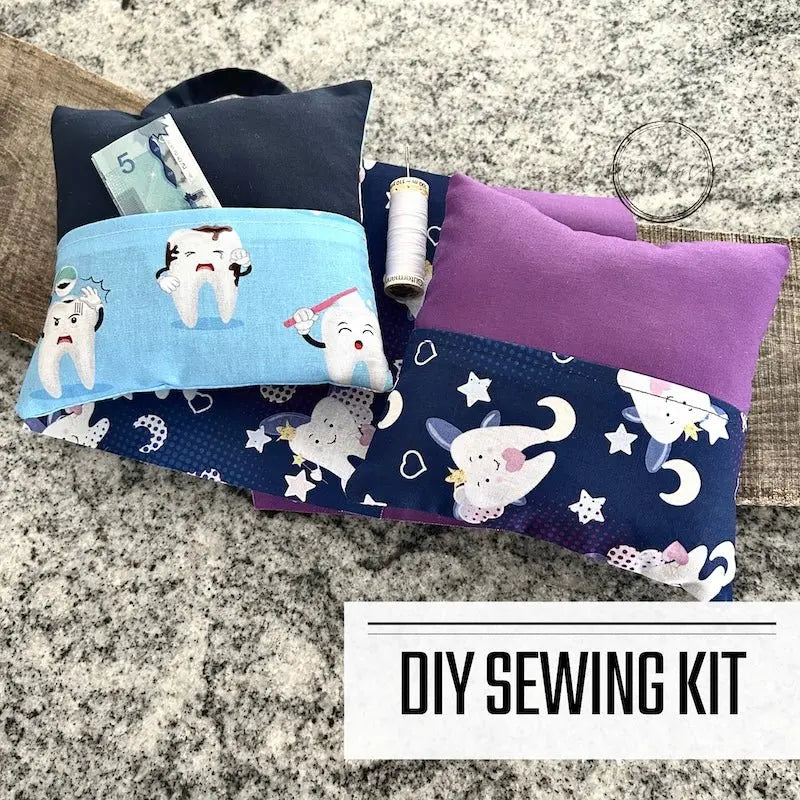 A DIY sewing kit for a tooth fairy pillow. The 2 pillows are lying on a wooden board on a counter.