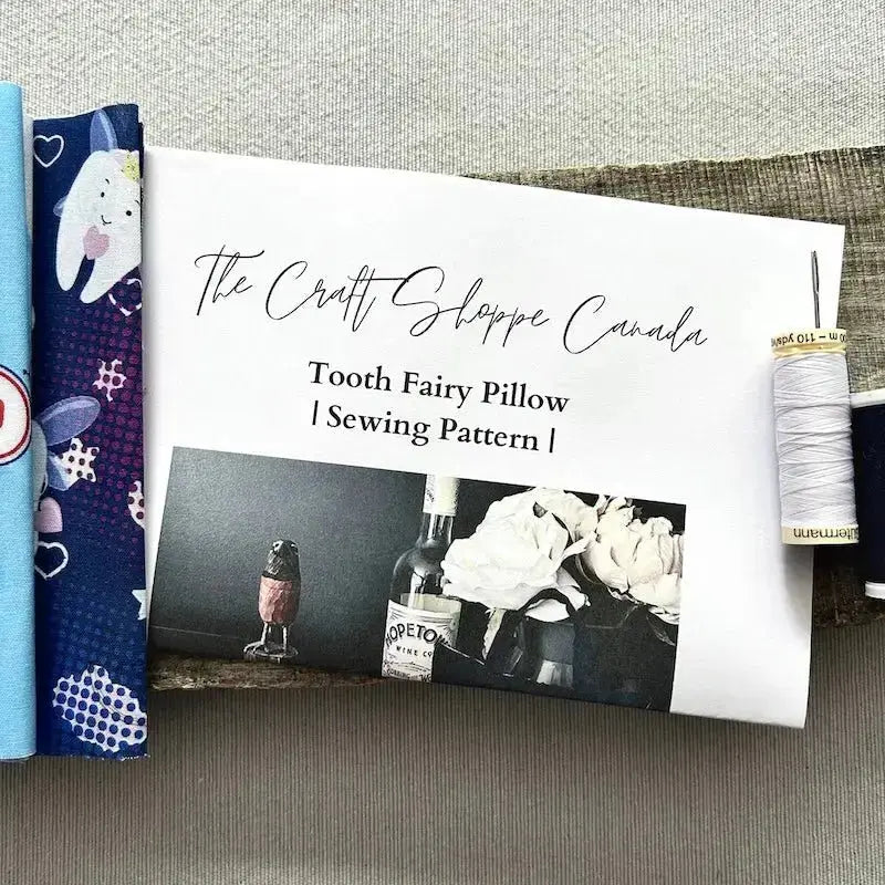 The pattern for this sewing kit is lying on a wooden board with fabric, a spool of thread and a hand sewing needle.