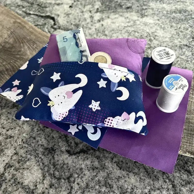 A tooth fairy pillow, from this sewing kit, is lying on a wooden board, with fabric and spools of thread.