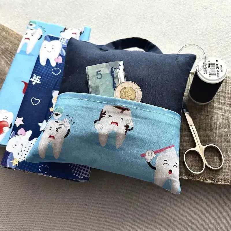 A tooth fairy pillow, from this sewing kit, is lying on a wooden board, with fabric and spools of thread.