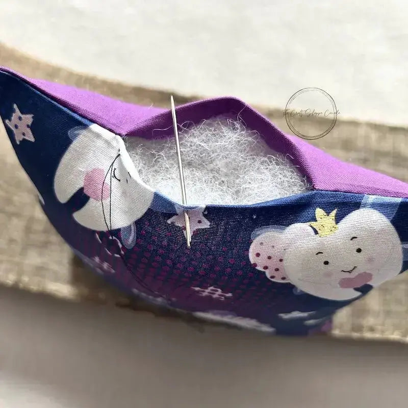 A close up of the top of the pillow, from this sewing kit, to show the stuffing inside with a tapestry needle closing up the top.