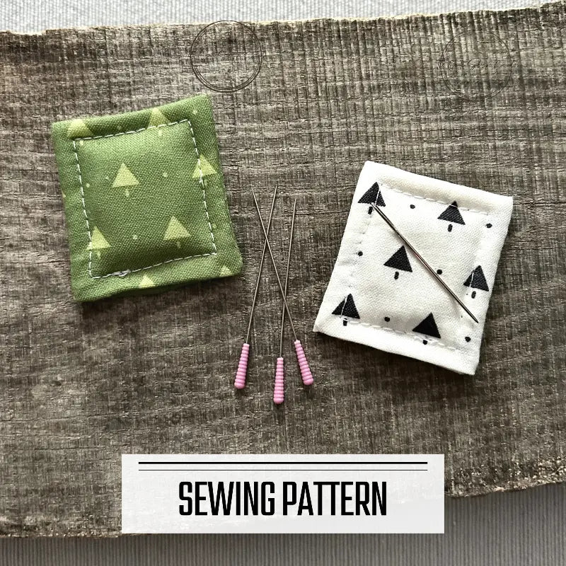A DIY sewing pattern for a needle minder/fridge magnet. There are 2 needle minders lying on a wooden board sewing pins and a sewing needle.