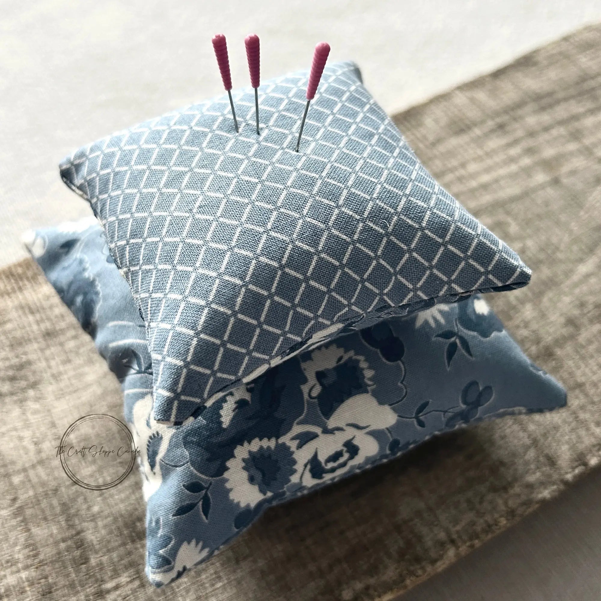 The finished pin cushions, made from this sewing pattern, are sitting on a wooden board with sewing pins on top.