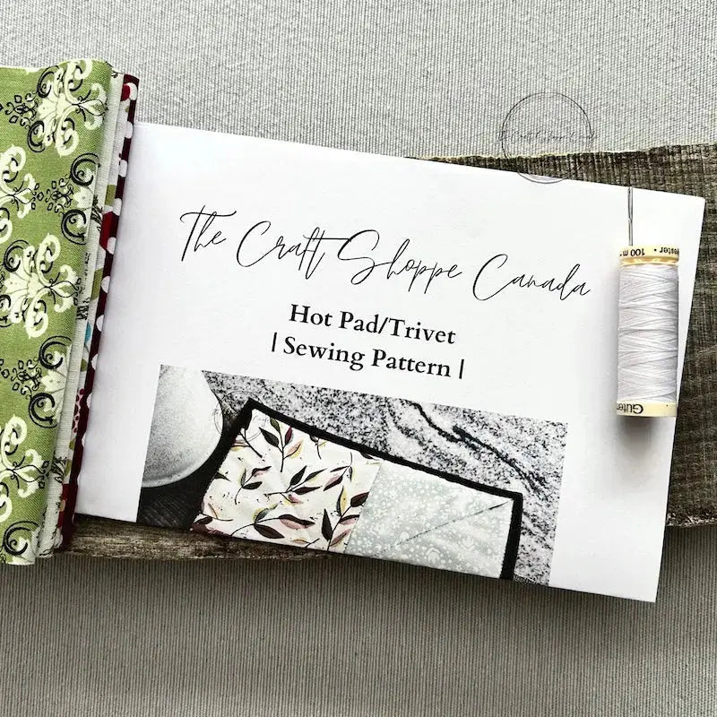 The pattern is lying on a wooden board with fabric, a spool of thread and a hand sewing needle.