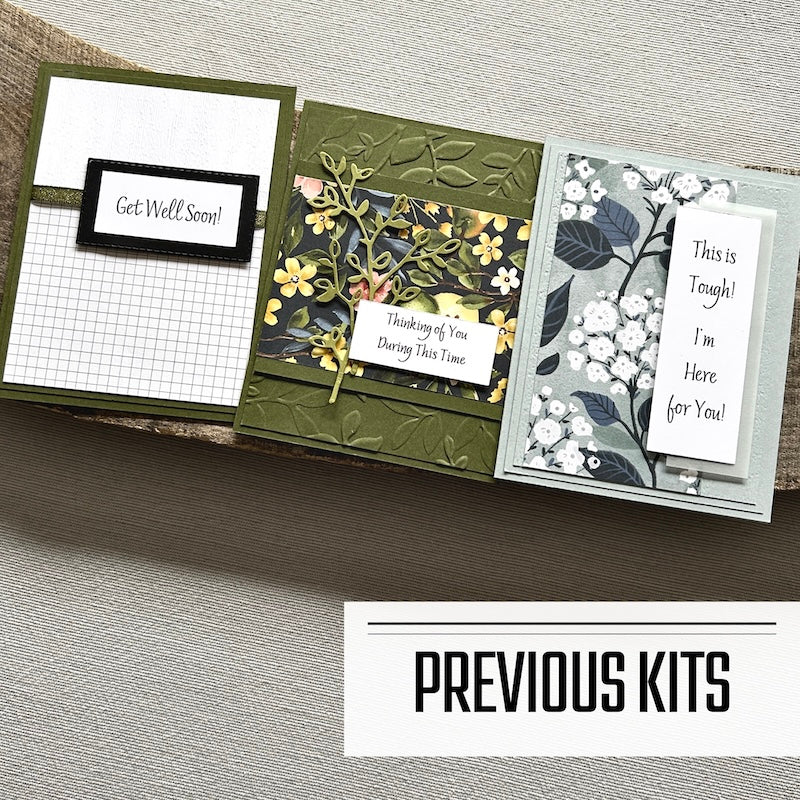 There are 3 finished cards, sitting on a wooden board, to show what cards have been sent in previous kits.