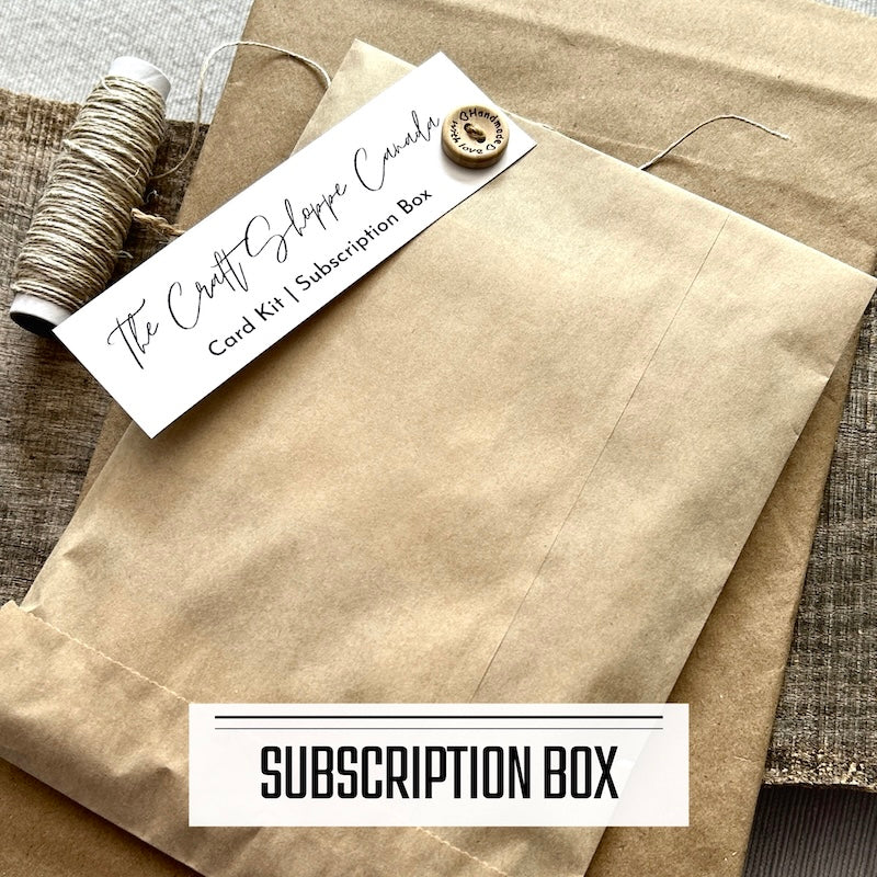 A monthly subscription box program featuring DIY card making kits. A subscription box envelope is sitting on a wooden board with a roll of twine.