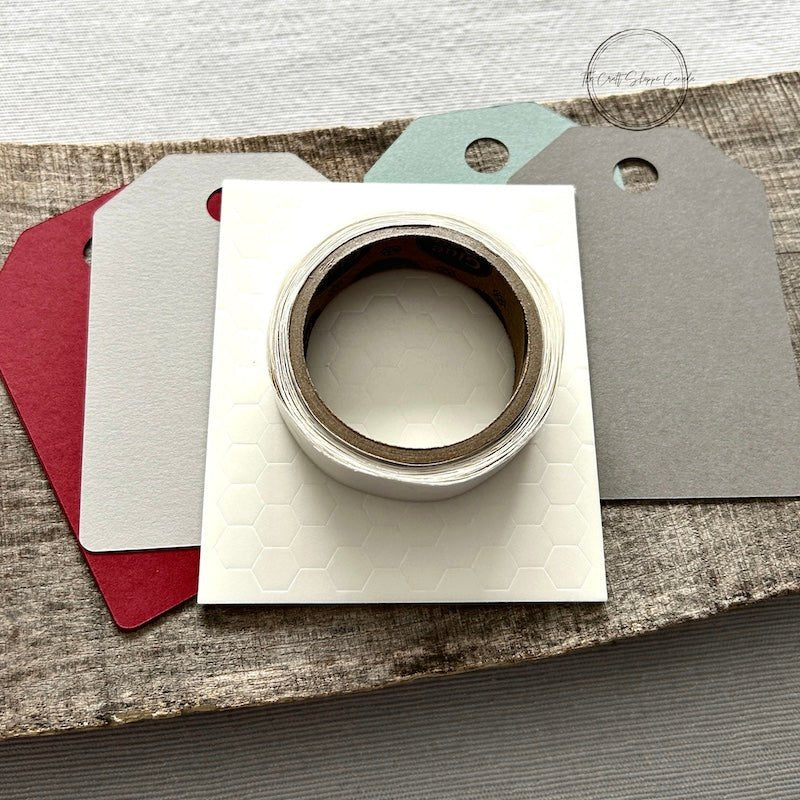 A DIY gift tag kit for Christmas. Finished tags are sitting on a wooden board with a roll of twine and a tape runner - The Craft Shoppe Canada 