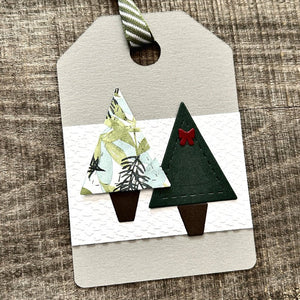 A finished gift tag, from this DIY kit, sitting on a wooden board.  - The Craft Shoppe Canada