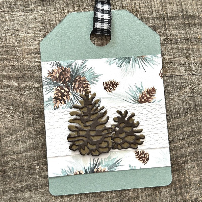 A finished gift tag, from this DIY kit, sitting on a wooden board.  - The Craft Shoppe Canada