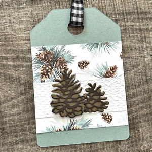 A finished gift tag, from this DIY kit, sitting on a wooden board.  - The Craft Shoppe Canada