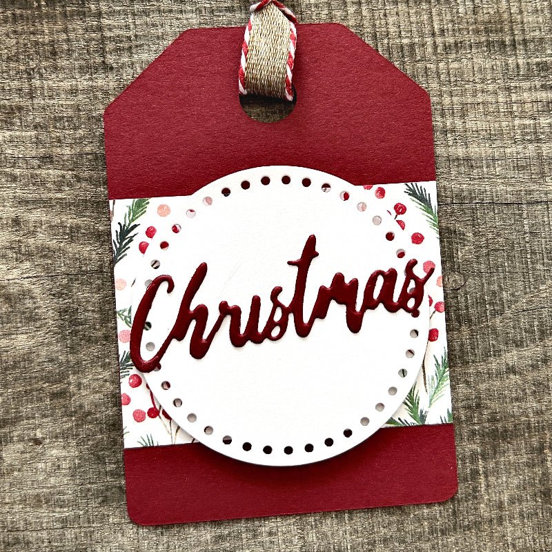 A finished gift tag, from this DIY kit, sitting on a wooden board.  - The Craft Shoppe Canada