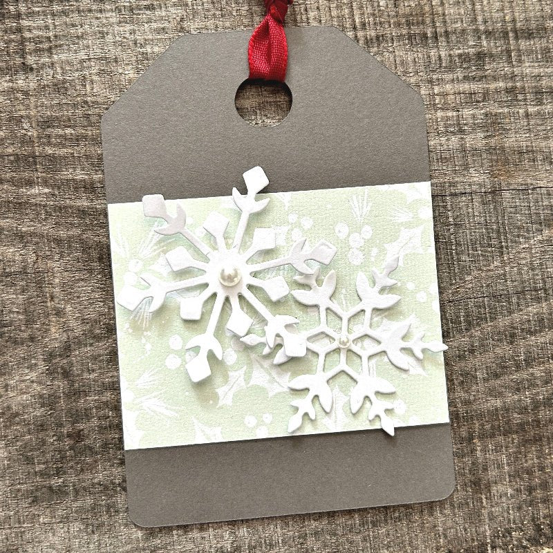 A finished gift tag, from this DIY kit, sitting on a wooden board.  - The Craft Shoppe Canada