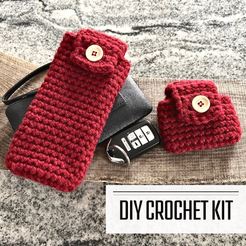 A DIY crochet kit for cases for our ear buds and eyeglasses. The cases are sitting on a wooden board with a wallet and keys- The Craft Shoppe Canada