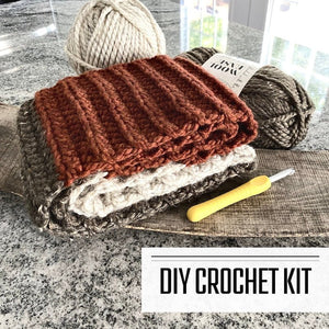 A crochet kit for a chunky knit fall scarf. The scarf is sitting on a wooden board with yarn and a crochet hook beside it - The Craft Shoppe Canada