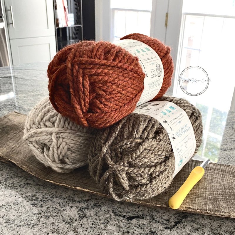 A close up of the orange, brown and ivory yarn on a wood board and a  crochet hook  - The Craft Shoppe Canada