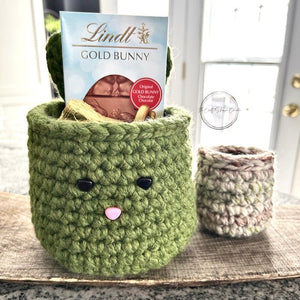 The crocheted Easter basket set sitting on a wooden board with chocolates inside and out of the baskets - The Craft Shoppe Canada