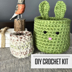 A DIY crochet kit for an Easter bunny basket set. The baskets are sitting on a buffet with a spring bird beside it - The Craft Shoppe Canada