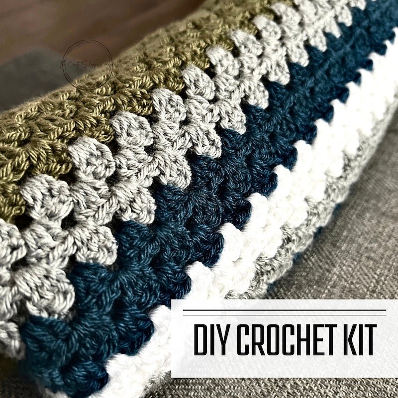 A DIY crochet kit for a couch throw or baby blanket. The finished blanket is rolled up on a couch - The Craft Shoppe Canada