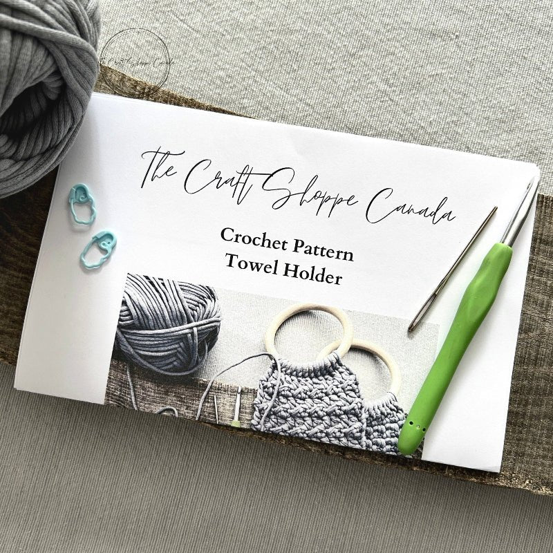 A copy of the towel holder pattern with a crochet hook, ball of yarn, a tapestry needle and 2 stitch markers - The Craft Shoppe Canada