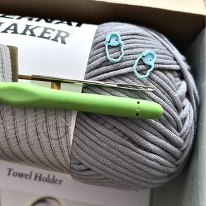 A ball of grey yarn in a box with a crochet hook, a tapestry needle and 2 stitch markets on it - The Craft Shoppe Canada