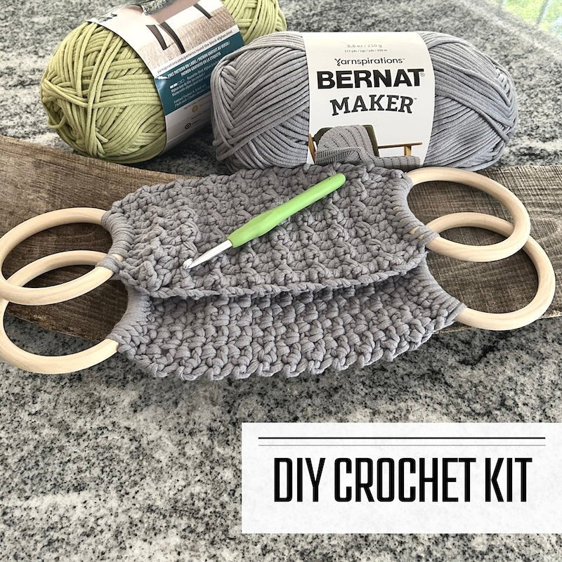 A DIY crochet kit for a tea towel holder. The holders are sitting on a wooden board with yarn and a crochet hook beside them - The Craft Shoppe Canada