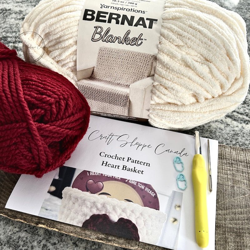 A DIY crochet kit for a Valentine’s heart-shaped basket, featuring white and red yarn, a crochet hook, and step-by-step instructions - The Craft Shoppe Canada