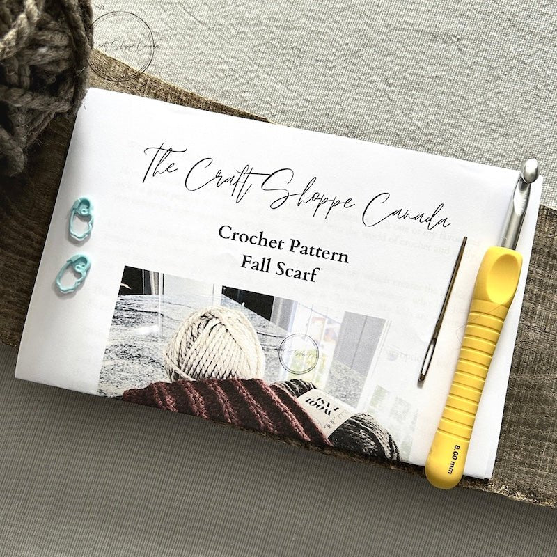 A copy of the wool scarf crochet pattern with a crochet hook, ball of yarn, a tapestry needle and 2 stitch markers - The Craft Shoppe Canada