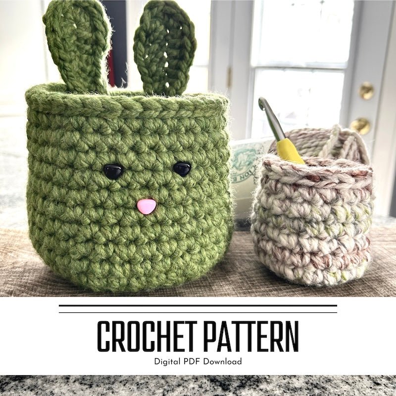 A crochet pattern for an Easter bunny basket set. The baskets are sitting on a wooden board with yarn and a crochet hook sitting in the smaller basket - The Craft Shoppe Canada