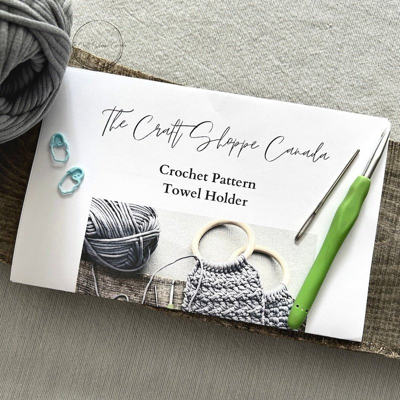 A copy of the towel holder pattern with a crochet hook, ball of yarn, a tapestry needle and 2 stitch markers - The Craft Shoppe Canada