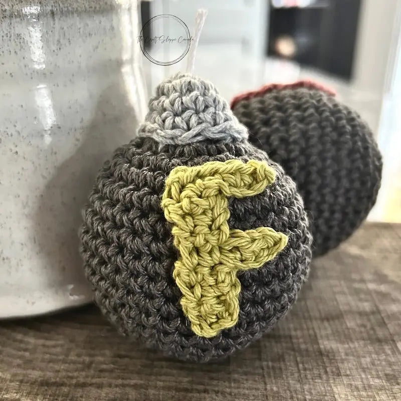 A close-up of the crochet F-Bomb plush leaning against a ceramic cup - The Craft Shoppe Canada