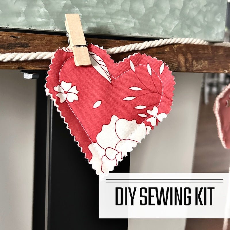 A DIY sewing kit for a valentine heart garland. The garland is hung over a table with flowers - The Craft Shoppe Canada