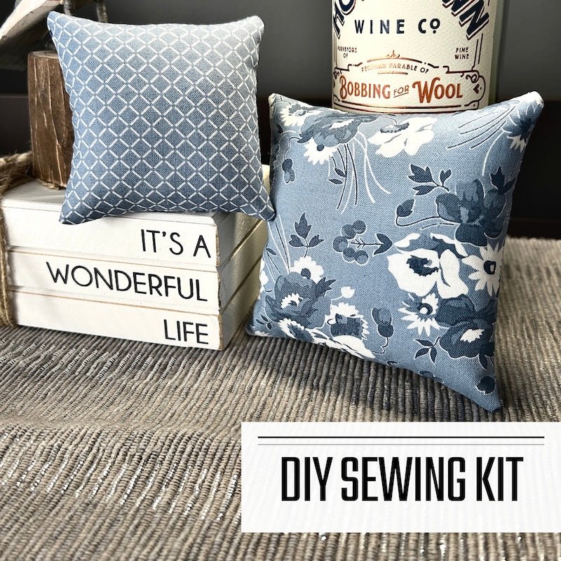 A DIY sewing pattern for a pin cushion set. There are 2 pin cushions sitting on a buffet with a bottle of wine and a decorative block - The Craft Shoppe Canada