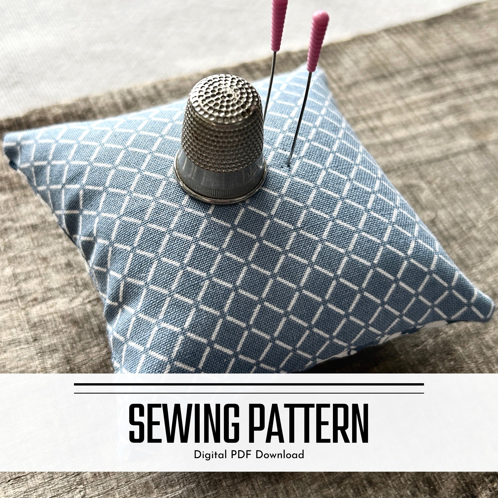 A digital sewing pattern for a pin cushion. The pin cushion is sitting on a wooden board with sewing pins stuck on top with a thimble - The Craft Shoppe Canada